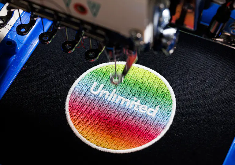 Stickmaschine stickt ein farbiges Logo-Emblem auf dunklen Stoff