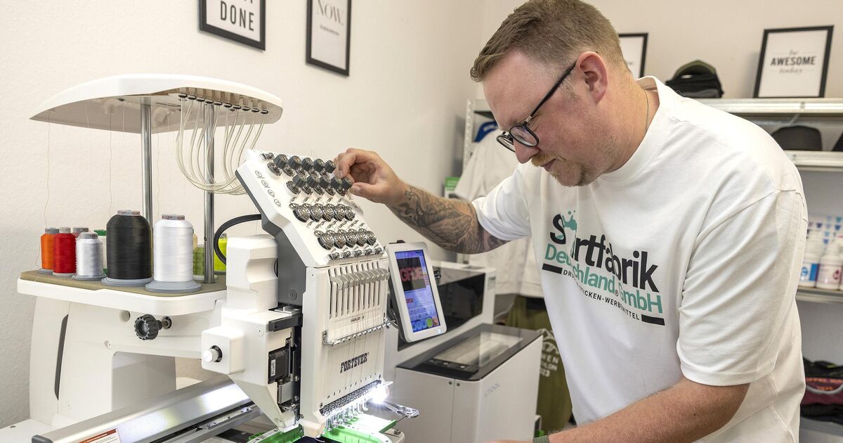 Mitarbeiter der Shirtfabrik Deutschland richtet eine Mehrnadel-Stickmaschine in der Werkstatt ein