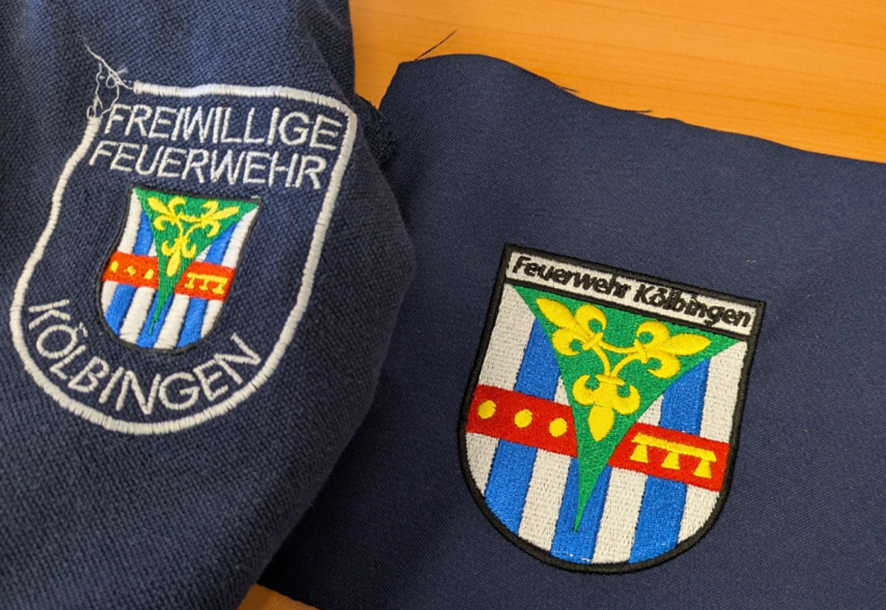 Zwei gestickte Wappen-Aufnäher auf dunkelblauem Textil im Vergleich