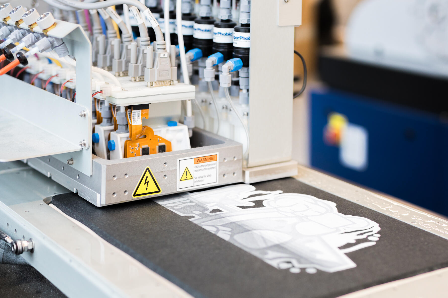 Digitaldruckmaschine druckt eine weiße Unterlage auf ein dunkles Textil in unserer Produktion